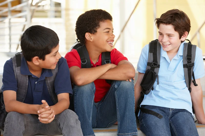 Three boys sitting together outside, smiling and talking